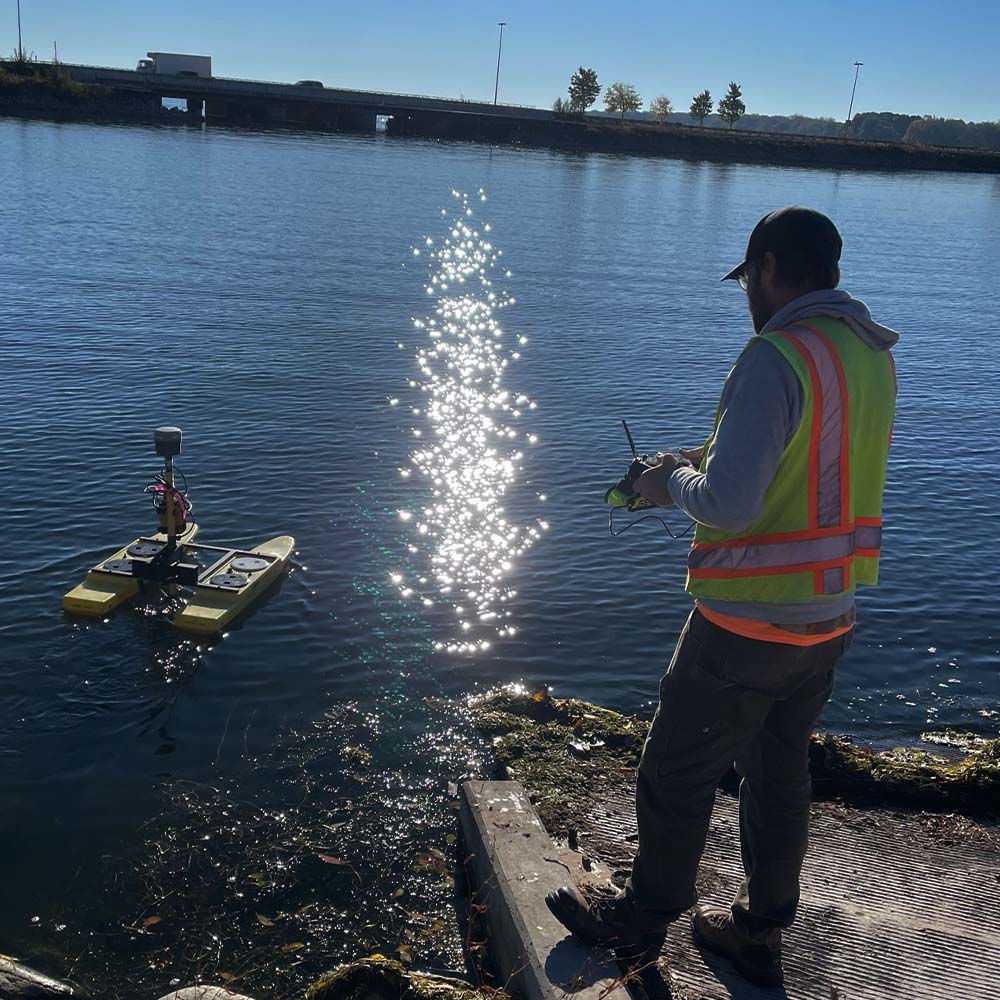 Person guiding a remote controlled survey equipment vessel on a body of water