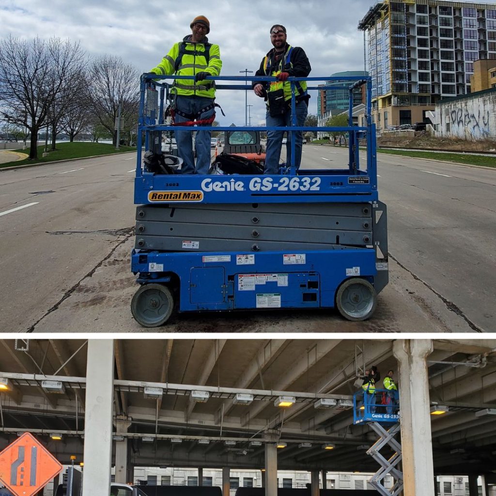 Top photo shows two men dressed in safety gear on top of a scissor lift in the middle of the street. Bottom photo shows same men on the lift while it's fully extended up to the top of the tunnel, under the Monona Terrace parking structure.