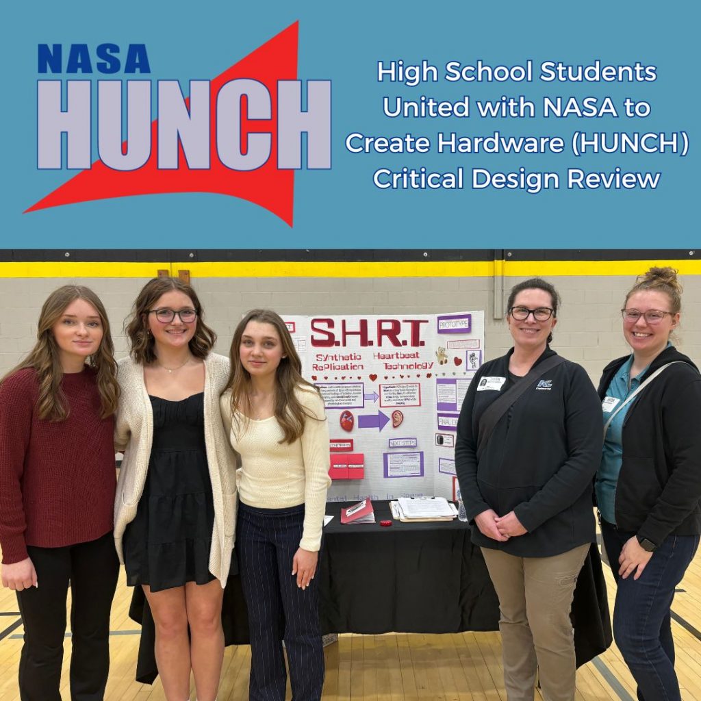 Photo of Samantha Herheim and Taylor Hopkins on right with 3 high school girls on the left, standing in front of their project table with NASA HUNCH logo overhead and 'High School Students United with NASA to Create Hardware (HUNCH) Critical Design Review' title at top of photo.