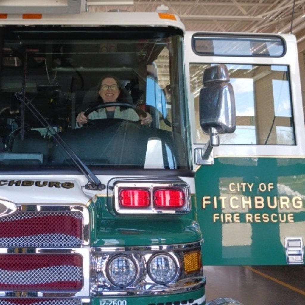 Photo of a green City of Fitchburg fire truck with Sam Herheim in the driver's seat with a huge grin!