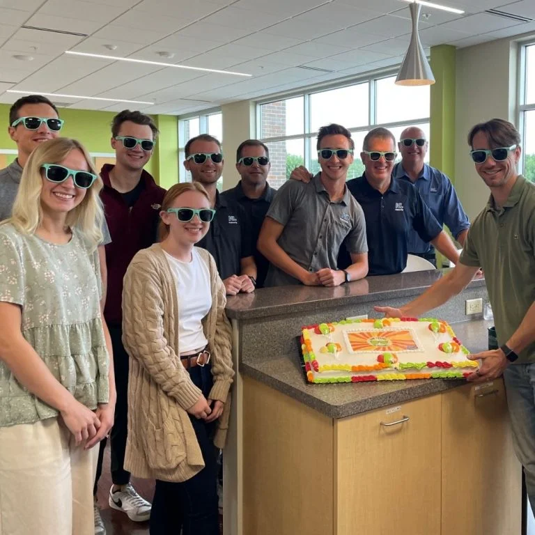 Group photo with staff wearing sunglasses with a 'Future is Bright' cake.