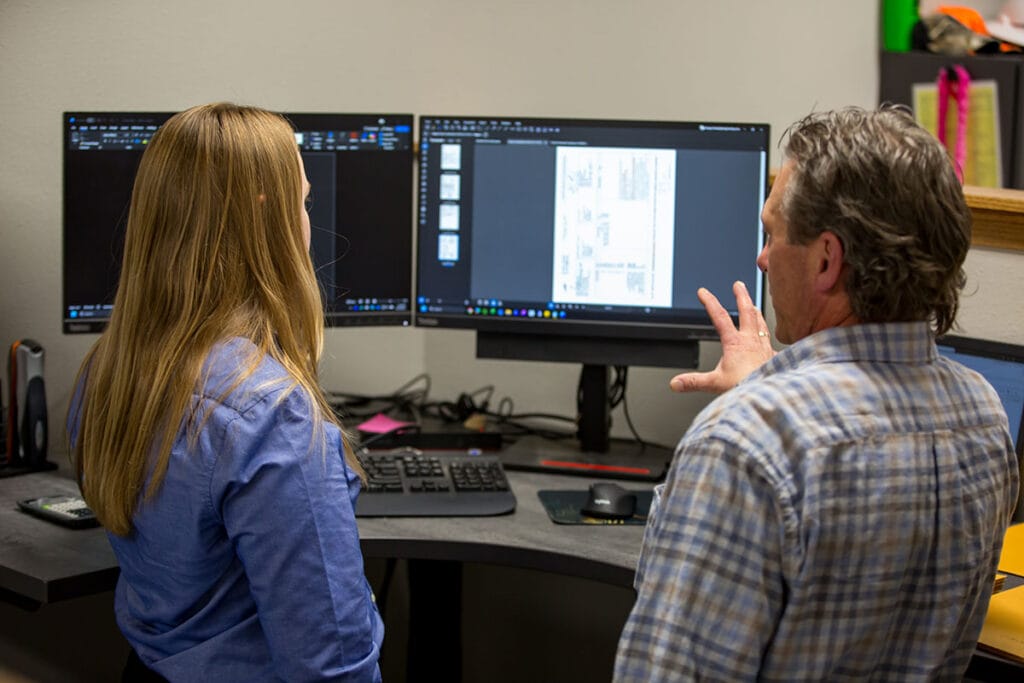 Two employees at a desk discussing what's on the computer screen.