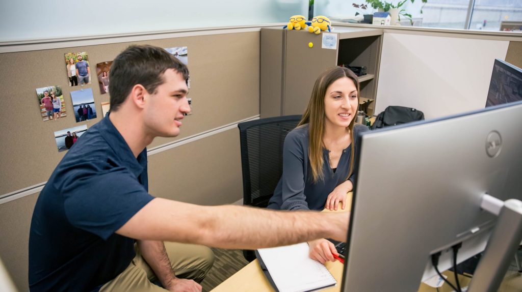 Two coworkers sitting at a desk looking at a computer together