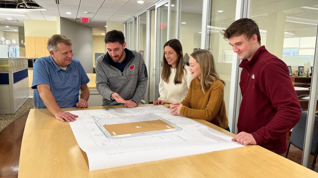 Site Development Team Five staff in a standing meeting in discussion, looking at plans on a table.