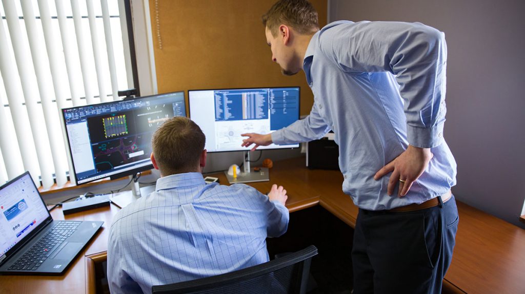 Two employees at a desk discussing what's on the computer screen.