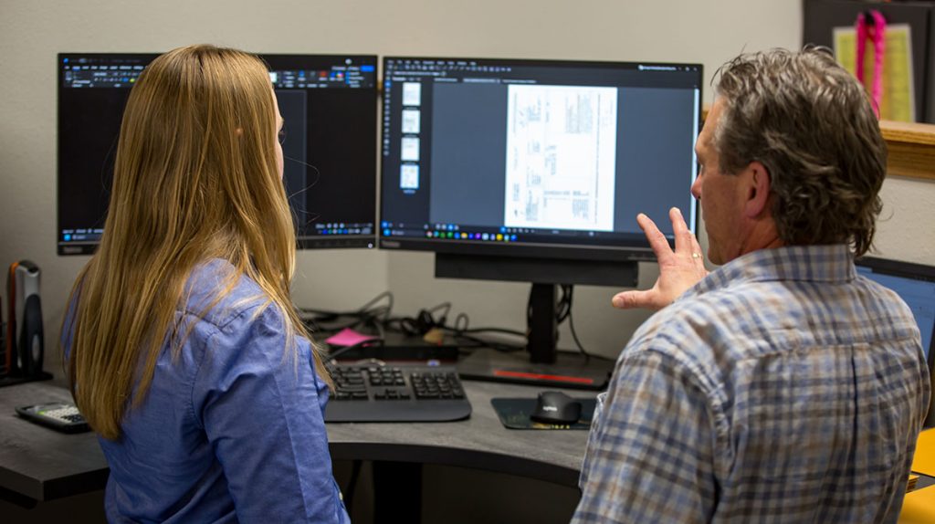 Two employees at a desk discussing what's on the computer screen.