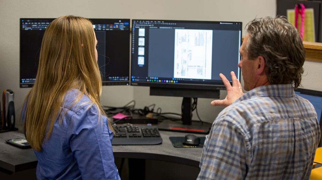 Two employees at a desk discussing what's on the computer screen.